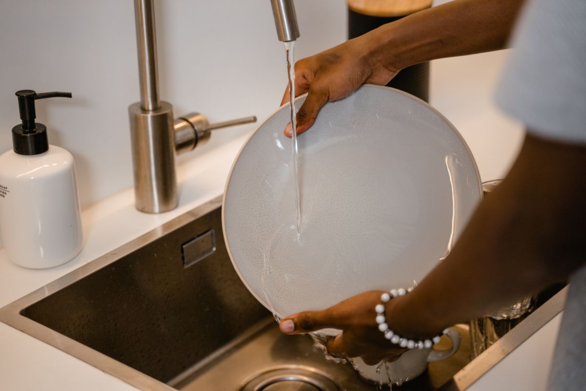 Hot water running at a kitchen sink while a plate is rinsed